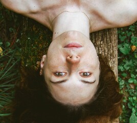 Upside down shot of a Caucasian woman laying on the tree trunk, looking straight.