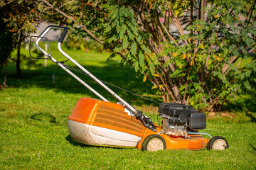 The lawn mower stands in a flowering garden after work. Mowing garden meadow lawn. Summer work in the garden, landscape design.