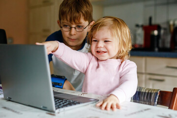 Cute little girl and school kid boy and looking at laptop, Two children, brother and sister using pc or notebook, e-learning on computer for kids. Siblings and family