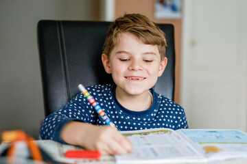 Happy smiling little kid boy in pajamas at home making homework at the morning before the school...