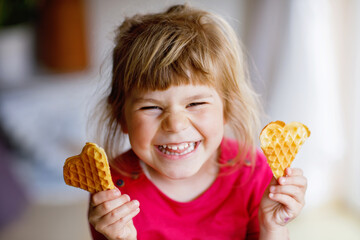 Portrait of happy little preschool girl holding fresh baked heart waffle. Smiling hungry toddler...