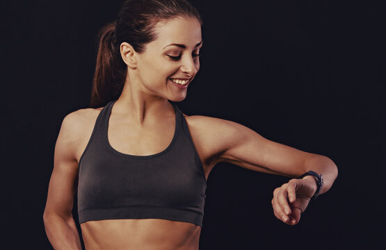 Happy smiling fit healthy fitness woman in bra top clothing looking on sporty watches what time is it now on black background with empty copy space. Closeup