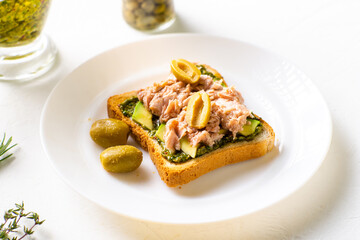 toast with tuna and avocado, olives with chimichurri sauce. On a white plate and white background.