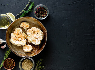 Cauliflower steak cooking. Raw cauliflower sprinkled with spices lies in a frying pan. Olive oil, herbs, various spices nearby. Dark background. Copyspace.