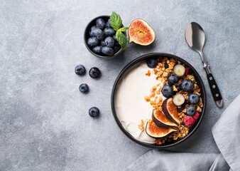 Natural yogurt with muesli, berries and figs in a black bowl on a blue background with napkin....