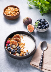 Natural yogurt with granola, berries and figs in a black bowl on a blue background with mint.