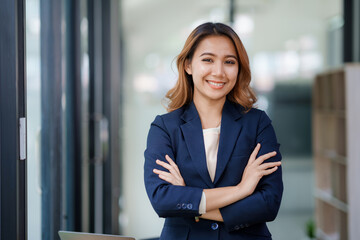 Pretty and confident young Asian business woman standing with her arms crossed and smiling brightly at the camera in the office. - Powered by Adobe