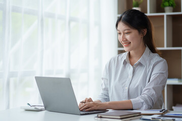 Portrait of smiling Asian businesswoman enjoying her work on her laptop at the office.
