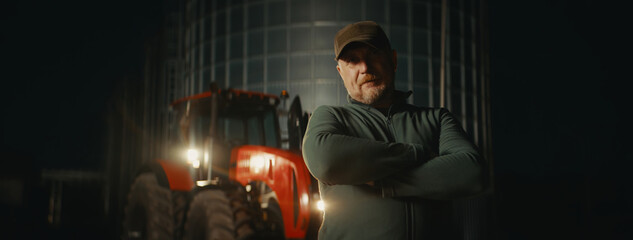 Hero shot portrait of 50s farmer posing on the farm near tractor early in the morning before...