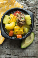 Sancocho, typical Colombian food in a black bowl on a rustic wooden background. Vertical photo.