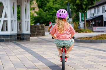 Little preschool girl with helmet running with balance bike on summer day. Happy child driving,...