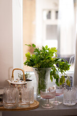 A picture of a table next to a windowsill with a vase of parsley and empty fizzio and old fashioned glasses