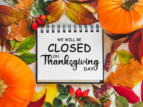 We will be closed for the Holidays. Beautiful Thanksgiving sign. Bright pumpkins, tree leaves, red berries and colorful flowers lying on an empty table. Close-up, top view. Holiday concept
