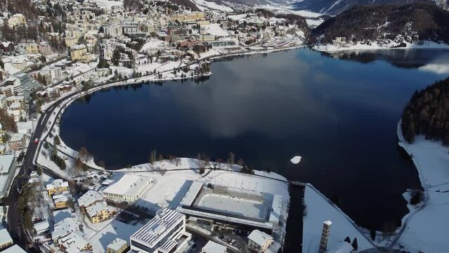 St Moritz, Switzerland: Aerial drone footage of the Saint Moritz ski resort village and lake on a sunny winter day in the Engadine valley in Canton Graubunden in the Swiss alps, with tilt up motion.