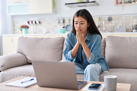 Nervous asian woman looking at laptop screen worrying about bad news