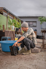 Caucasian male putting soil in black garden pots for gardening with his Jack Russell Terrier dog, Cape Town, South Africa