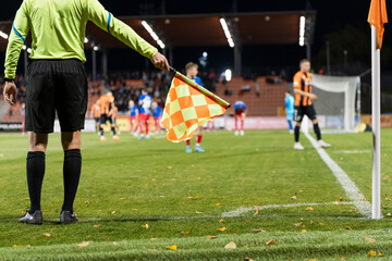 Soccer touchline referee with the flag shows corner during match at the football stadium.