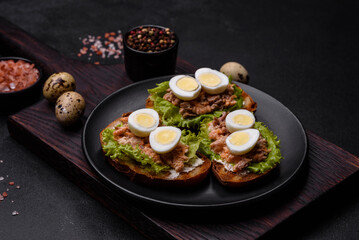 Fototapeta na wymiar Delicious fresh sandwiches with toast, canned salmon, salad and quail eggs