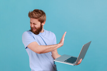 Portrait of handsome bearded man showing stop gesture, avoiding watch something unpleasant, turning...