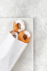 Donuts with powdered sugar in craft Paper bag for food on grey background. Take away food, place for text.