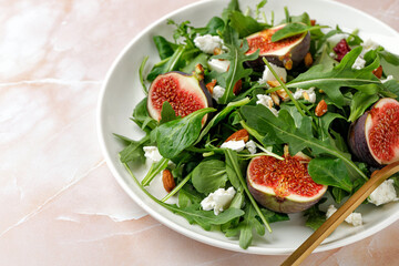 Healthy Salad with figs, arugula, feta cheese on a white plate on pink beige marble background.