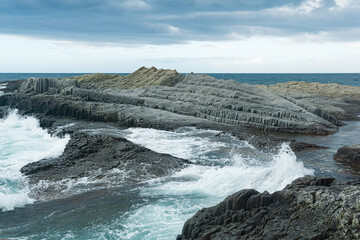 rocky seashore formed by columnar basalt against the backdrop of a stormy sea, coastal landscape of the Kuril Islands