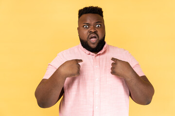 Portrait of bearded astonished man wearing pink shirt pointing at himself, asks who me, has...