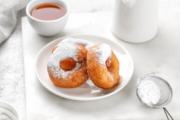 Donuts with powdered sugar and cup of tea. Circle Donuts fried in oil without icing. Doughnut pastry, potato donuts. Pyshki.