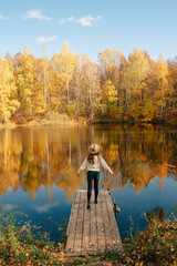 A young girl in a hat stands on a bridge near a pond in an autumn landscape