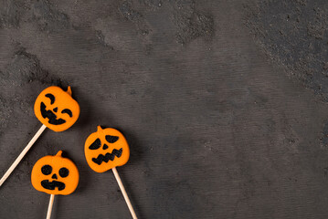 Themed Pumpkin jelly candies on a wooden stick. Halloween. Dark background. Top view. Copy space	