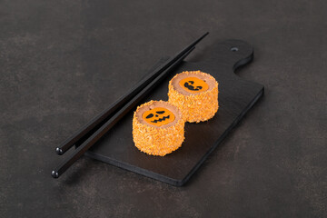 Small round mousse cake with pumpkin jelly and colored sprinkles, on a serving board. Halloween holiday. Dark background	