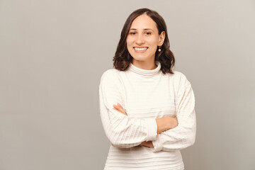 Fototapeta premium Portrait of a smiling confident woman standing with crossed arms in a studio over grey background.