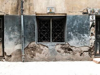 Closeup of the small square window of an old building with its walls deteriorating - obrazy, fototapety, plakaty