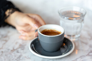 Espresso cup in female hands and glass of water on the table. Morning ritual at the cafe.