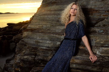 Beautiful blonde dress girl posing on beach. Long curly hair and stylish dress.