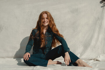 Beautiful cheerful redhead girl with long curly hair smiling over beige background.