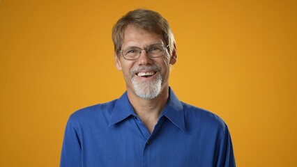 Smiling cheerful laughing mature bearded man in blue shirt isolated on solid yellow background...