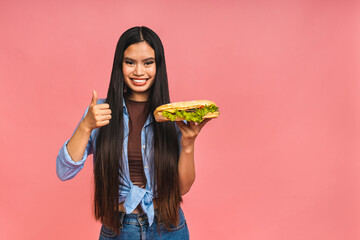 Young beautiful asian japanese chinese woman eating sandwich or big burger with satisfaction. Girl enjoys tasty hamburger takeaway, diet concept, standing isolated over pink background. - Powered by Adobe
