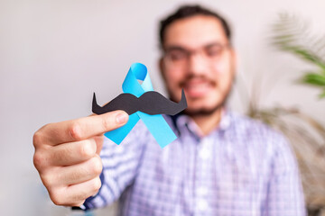 Man Hands holding blue ribbon and paper mustache. Prostate Cancer Awareness, November blue,....