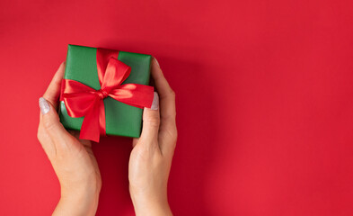 Woman hands holding Christmas present. Gift box wrapped in green paper with red ribbon.