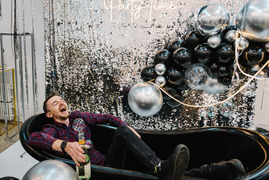 Happy man with champagne in black bath celebrating new 2023 year. Place for congratulations for birthday. Arch or photo booth decorated silver balloons. Wall, zone for photography. Text party time.