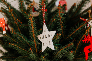 Christmas tree with different wooden decorations. Christmas garland and Christmas lights. White and red colors. Christmas deer, star, snowflake, Bullfinch