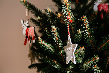 Christmas tree with different wooden decorations. Christmas garland and Christmas lights. White and red colors. Christmas deer, star, snowflake. Rays of sunlight fall on the fir branches