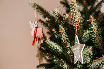 Christmas tree with different wooden decorations. Christmas garland and Christmas lights. White and red colors. Christmas deer, star, snowflake. Rays of sunlight fall on the fir branches