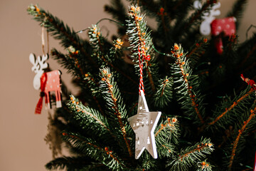 Christmas tree with different wooden decorations. Christmas garland and Christmas lights. White and red colors. Christmas deer, star, snowflake. Rays of sunlight fall on the fir branches