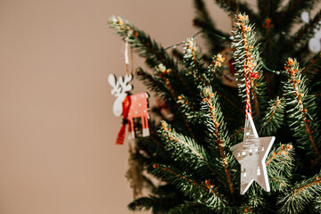 Christmas tree with different wooden decorations. Christmas garland and Christmas lights. White and red colors. Christmas deer, star, snowflake. Rays of sunlight fall on the fir branches