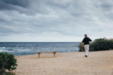 Un homme marchant sur une plage de la Côte-d'Azur. La Côte-d'Azur en hiver. Un homme et un banc vide au bord de la mer.