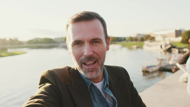 Close up, man makes video call on mobile phone on the embankment of the river. Backlight