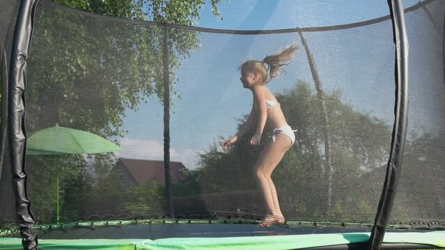 Cute little girl in a swimsuit is jumping and having fun on the trampolin