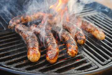 Gegrillte Allgäuer Bratwurst angeboten als close-up auf einem Holzkohlegrill mit Feuer und Rauch